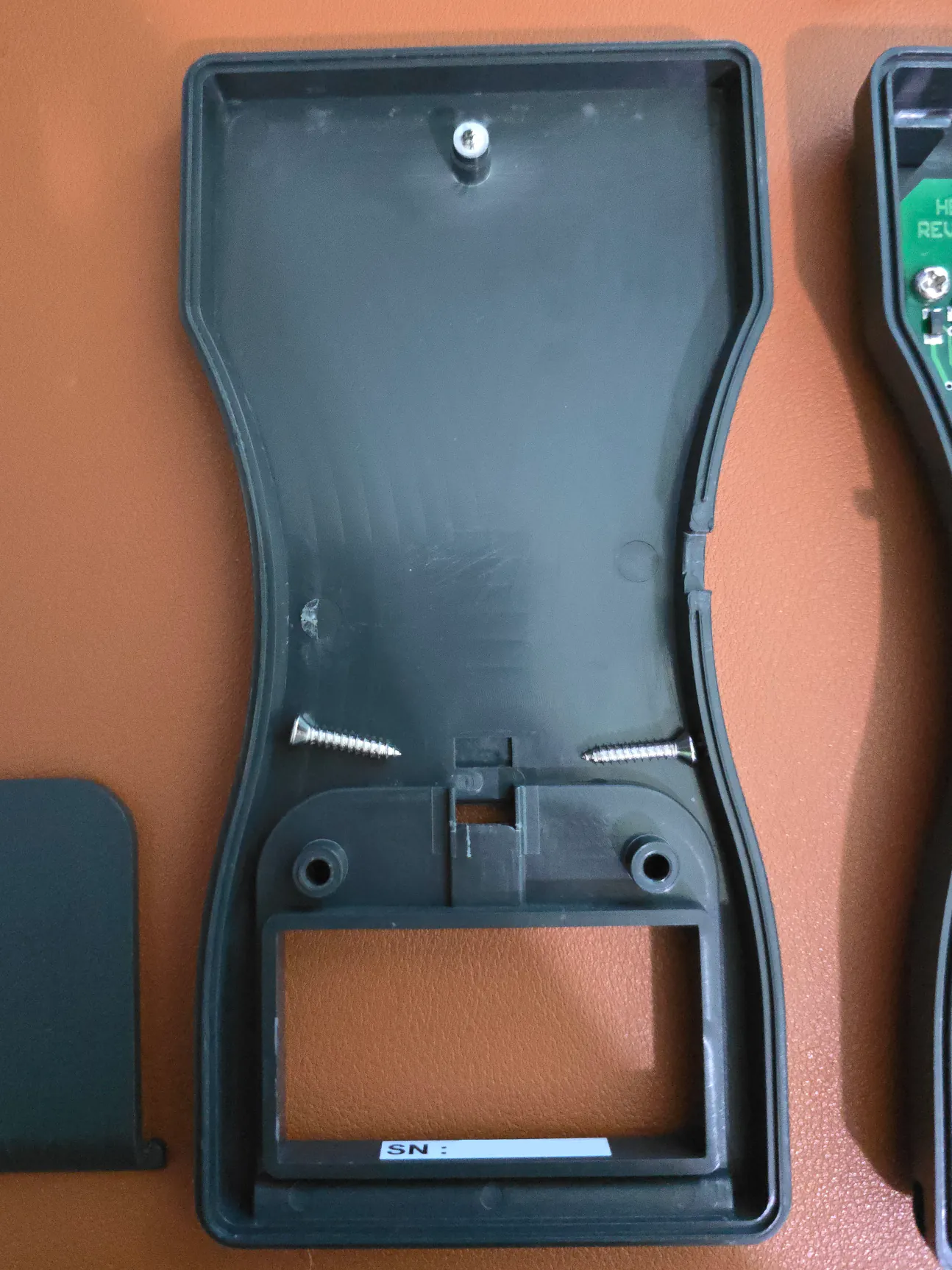 the bottom half of the enclosure, with two loose screws at bottom and one screw in the boss.
